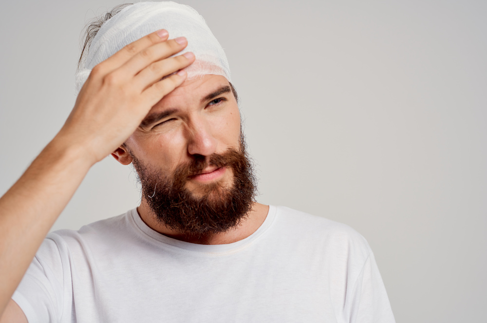 A man holding his bandaged head in pain after having being diagnosed with a brain injury.