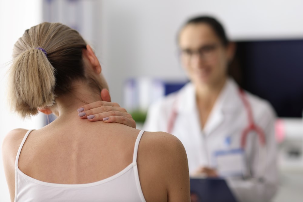 A woman touching her neck to show her doctor where she is feeling pain.