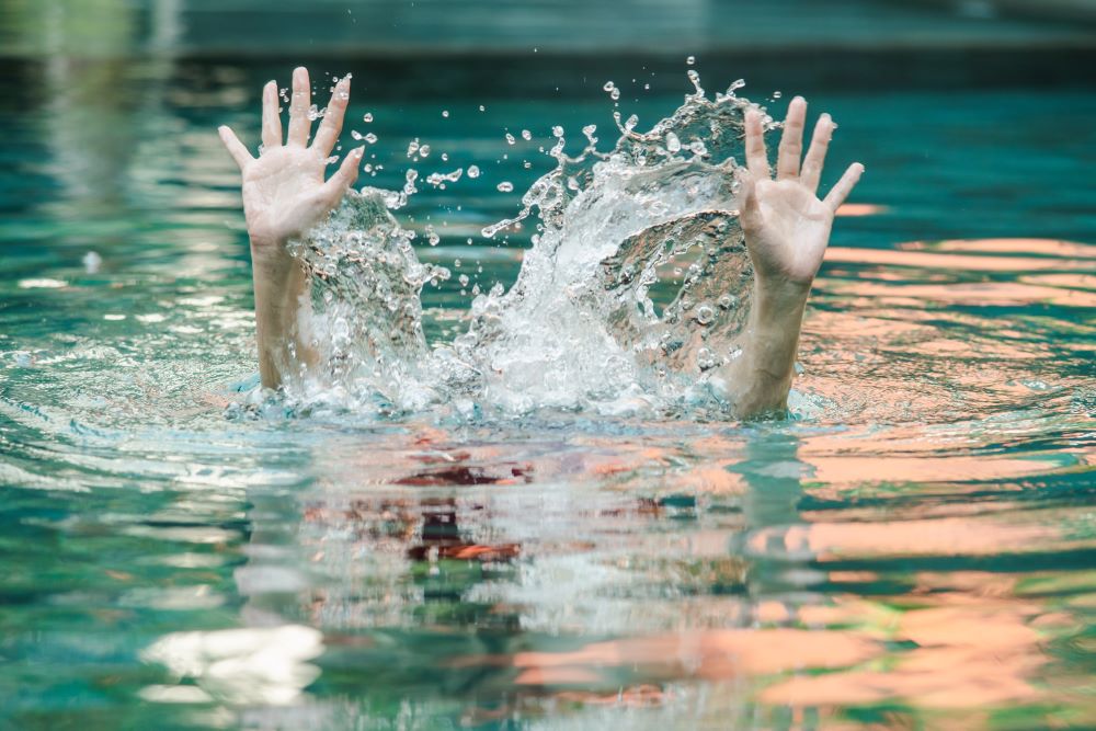 A person struggling to swim waving their hands in the air to alert others they might be drowning.