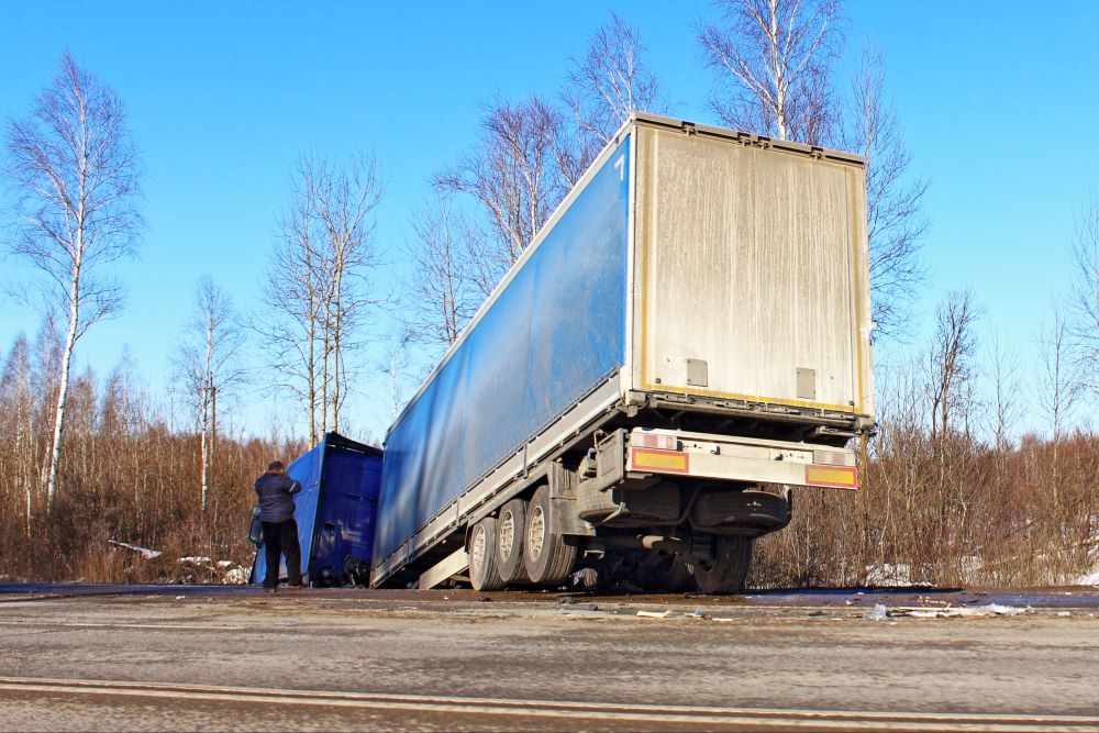 A truck driver assessing the damage after a semi-truck accident on the highway.