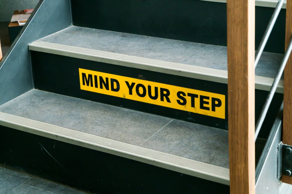 A warning sign placed on a staircase in a retail store instructing customers to mind their step when walking on the stairs.