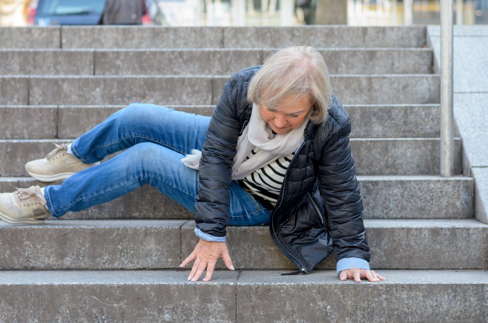 An elderly woman struggling to get up after a slip down the stairs in a public area.
