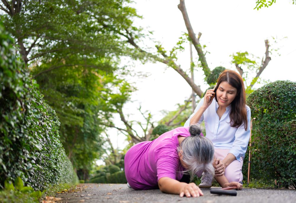 A woman on the phone with emergency services while helping an elderly woman who has fallen.